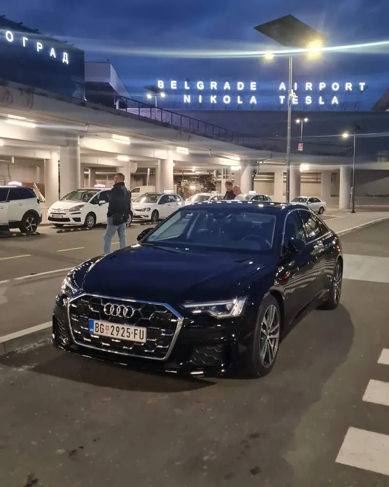 Passenger Transfers Audi A6 outside the Nikola Tesla Airport terminal at night